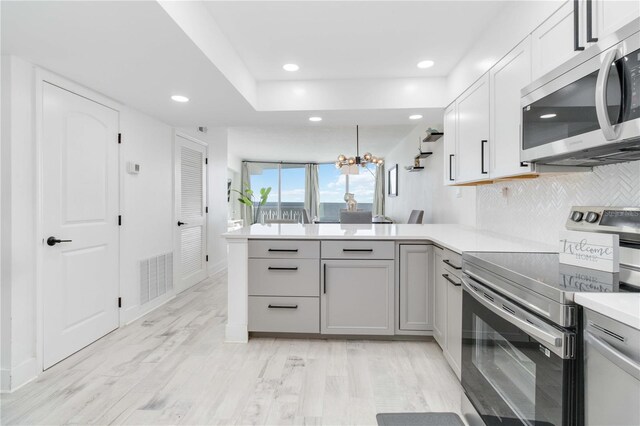 kitchen featuring decorative backsplash, light hardwood / wood-style flooring, kitchen peninsula, an inviting chandelier, and appliances with stainless steel finishes