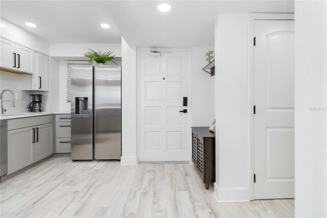 kitchen featuring stainless steel refrigerator with ice dispenser, gray cabinetry, backsplash, sink, and light hardwood / wood-style floors