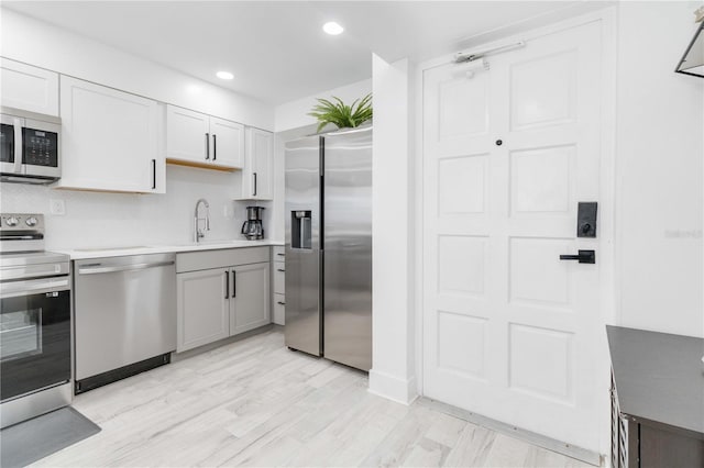 kitchen with decorative backsplash, appliances with stainless steel finishes, white cabinetry, light hardwood / wood-style flooring, and sink