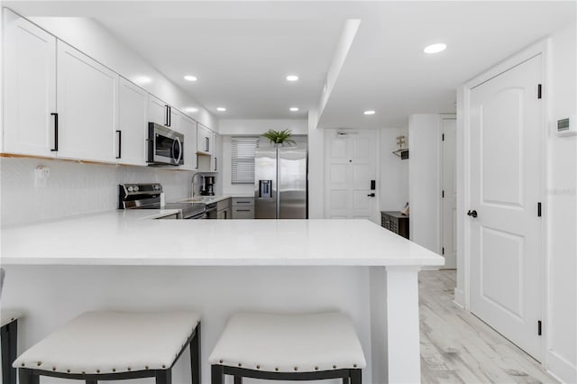 kitchen featuring stainless steel appliances, a breakfast bar area, kitchen peninsula, and white cabinets