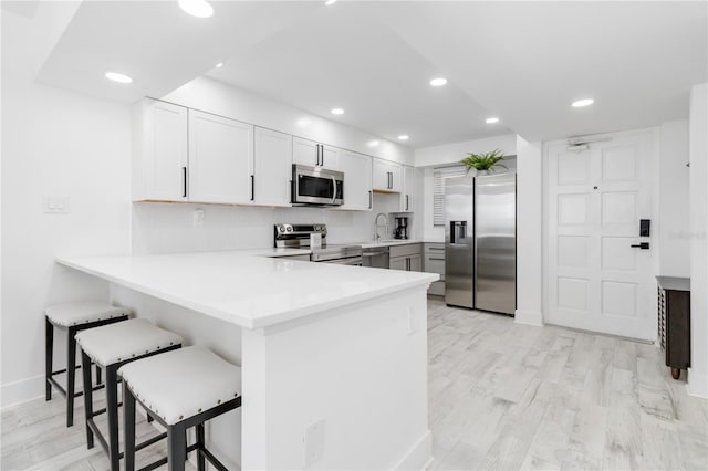 kitchen with kitchen peninsula, white cabinets, a kitchen breakfast bar, light hardwood / wood-style floors, and stainless steel appliances