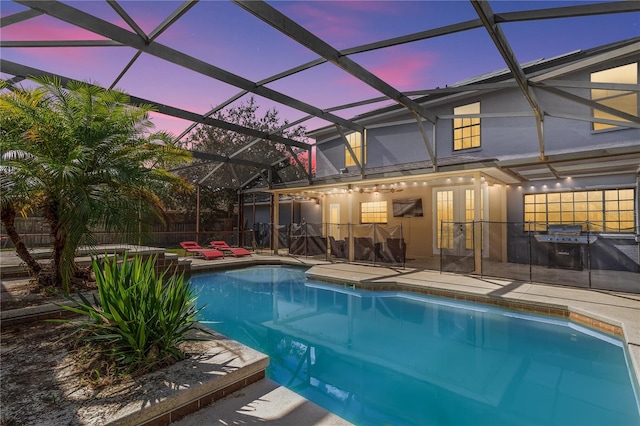 pool at dusk with a patio, glass enclosure, and a jacuzzi