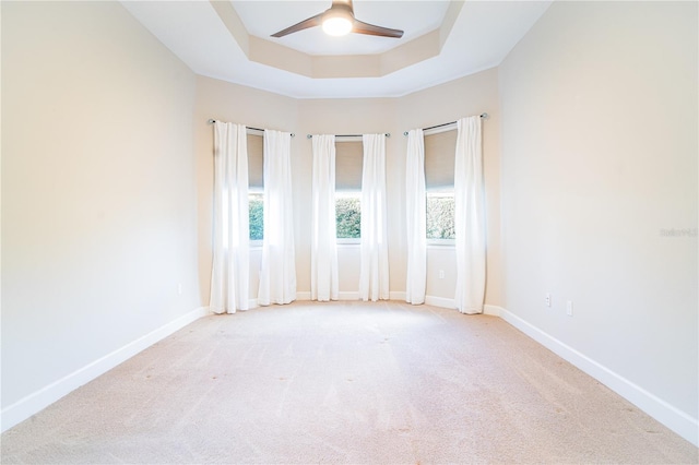 empty room featuring light carpet, a tray ceiling, and ceiling fan