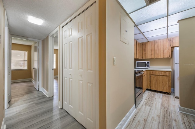 hall with light hardwood / wood-style flooring, a textured ceiling, and electric panel