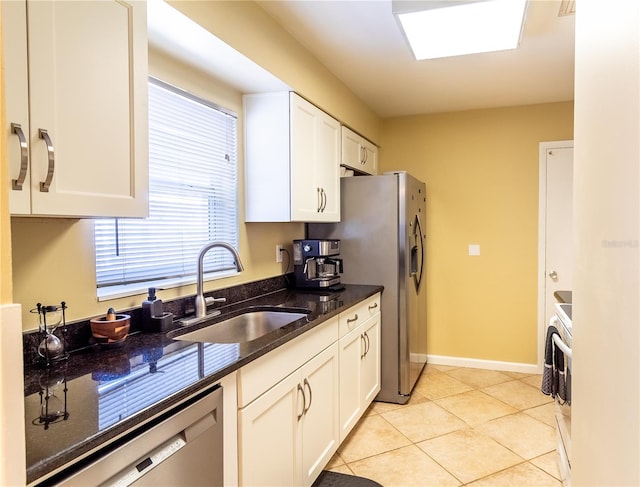 kitchen with appliances with stainless steel finishes, light tile patterned flooring, sink, dark stone counters, and white cabinets