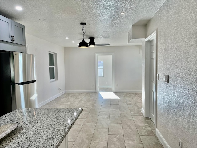 kitchen featuring a textured ceiling, ceiling fan, gray cabinets, light stone counters, and stainless steel refrigerator