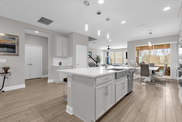 kitchen featuring an island with sink, hanging light fixtures, white cabinets, and light hardwood / wood-style floors