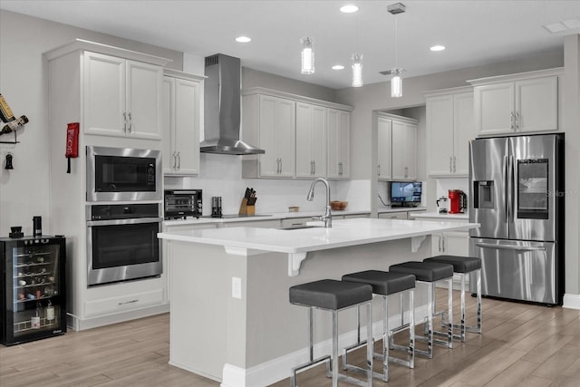 kitchen with wall chimney range hood, light hardwood / wood-style floors, stainless steel appliances, white cabinets, and wine cooler