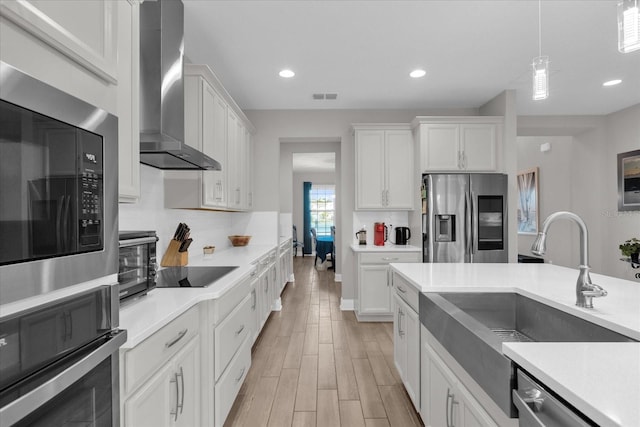 kitchen featuring hanging light fixtures, stainless steel appliances, wall chimney exhaust hood, and white cabinets