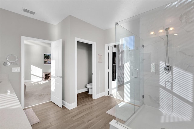 bathroom with toilet, a shower with shower door, and hardwood / wood-style floors