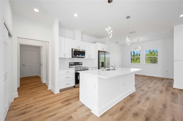 kitchen featuring light wood-type flooring, stainless steel appliances, decorative light fixtures, a center island with sink, and white cabinetry