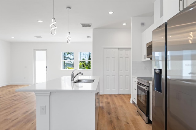 kitchen with white cabinets, pendant lighting, stainless steel appliances, and light hardwood / wood-style floors