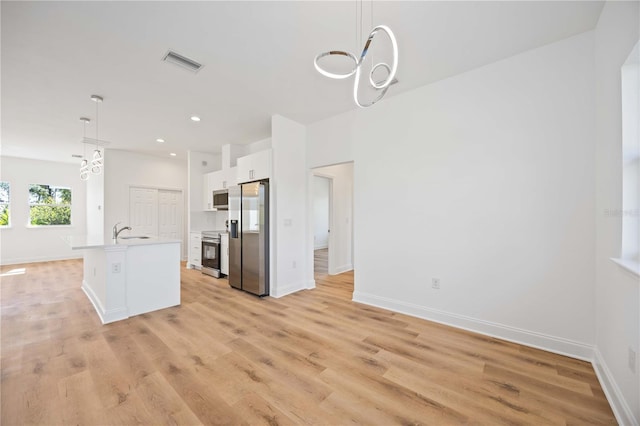 kitchen featuring light wood-type flooring, stainless steel appliances, a center island with sink, white cabinets, and hanging light fixtures