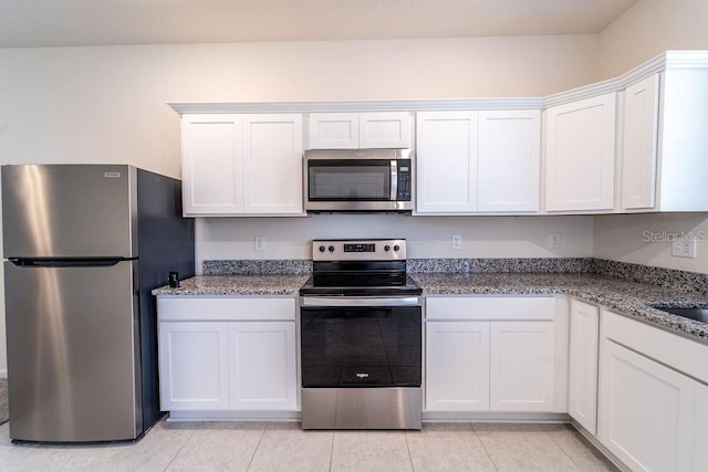 kitchen with white cabinetry, stainless steel appliances, light stone counters, and light tile patterned floors