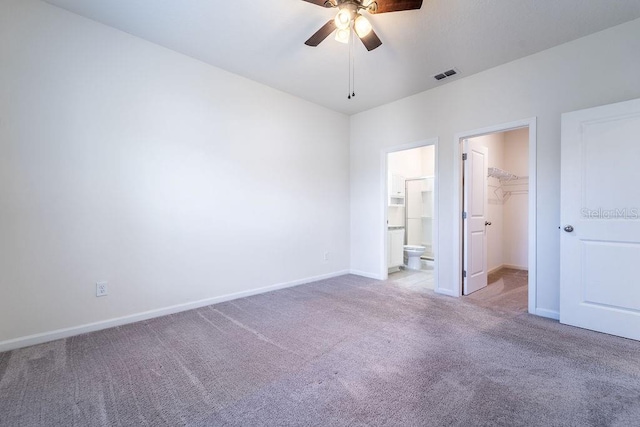 unfurnished bedroom featuring a closet, ensuite bath, a spacious closet, carpet flooring, and ceiling fan