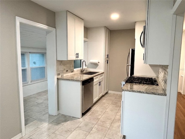 kitchen featuring light stone countertops, sink, appliances with stainless steel finishes, backsplash, and white cabinetry