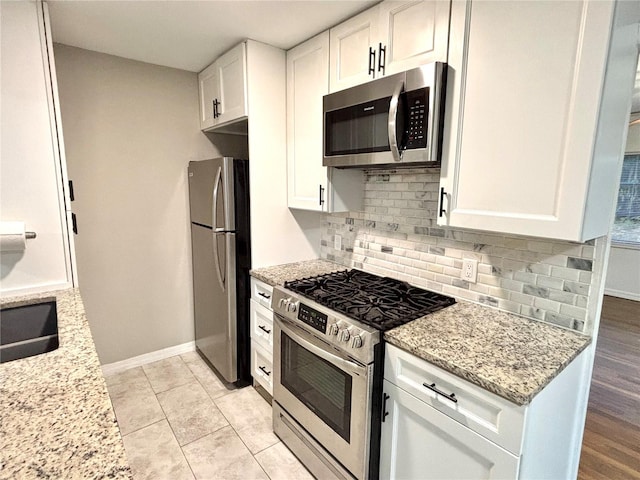 kitchen featuring appliances with stainless steel finishes, light stone counters, white cabinetry, and tasteful backsplash