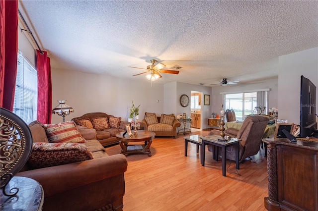 living room with ceiling fan, a textured ceiling, and light hardwood / wood-style flooring