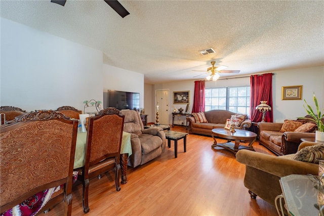 living room featuring a textured ceiling, light wood-type flooring, and ceiling fan