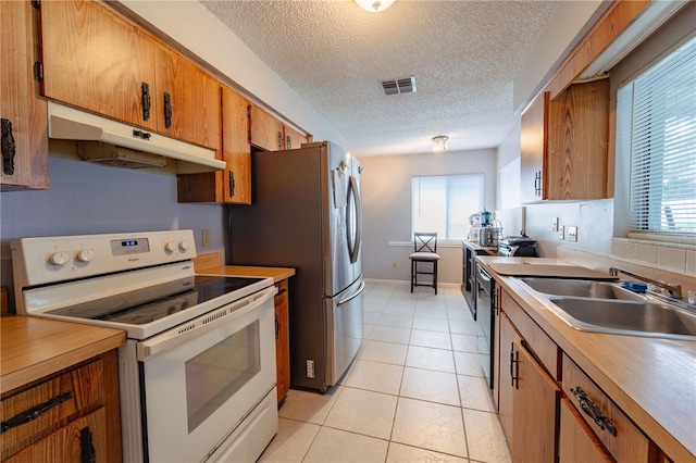 kitchen with a textured ceiling, appliances with stainless steel finishes, sink, and light tile patterned flooring