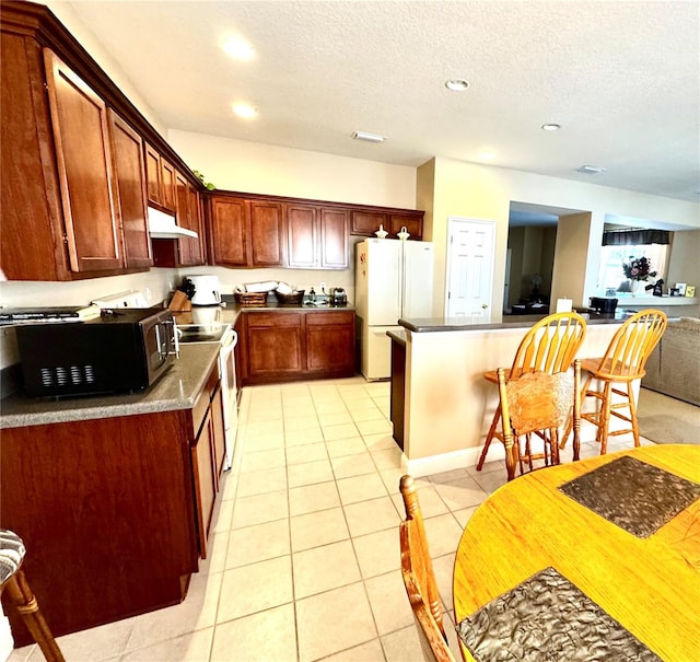 kitchen with a textured ceiling, light tile patterned flooring, and white appliances