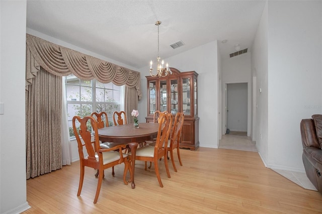 dining space with light hardwood / wood-style floors, a textured ceiling, and an inviting chandelier