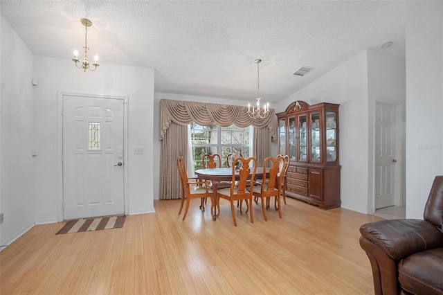 dining room with light hardwood / wood-style flooring, a textured ceiling, and a chandelier