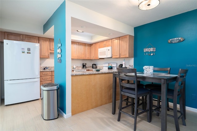 kitchen with light stone countertops, white appliances, and a raised ceiling