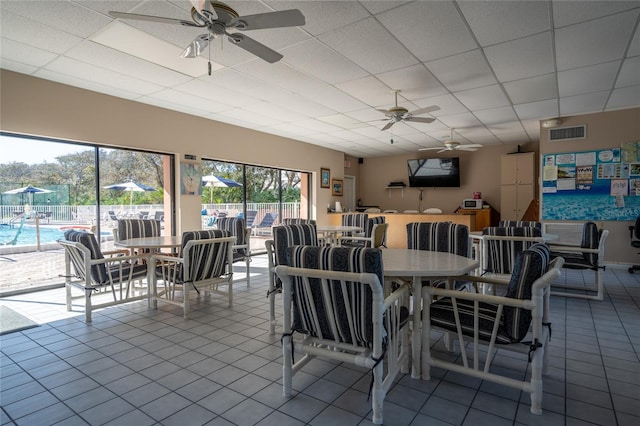 dining room featuring ceiling fan, a drop ceiling, and tile patterned flooring