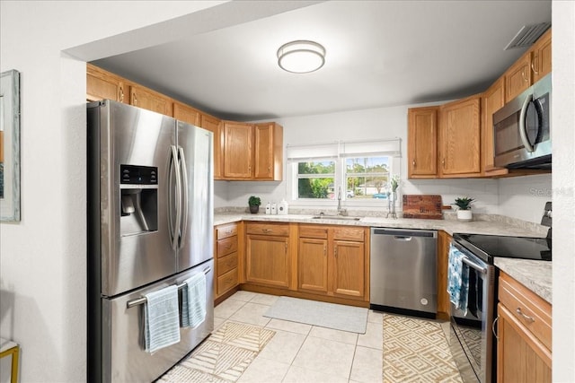 kitchen with light stone countertops, appliances with stainless steel finishes, sink, and light tile patterned floors