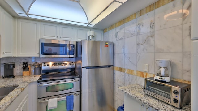 kitchen with white cabinets, decorative backsplash, light stone countertops, and appliances with stainless steel finishes