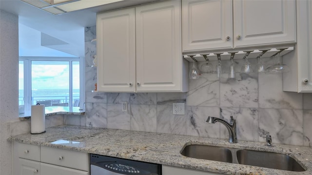 kitchen with light stone countertops, tasteful backsplash, stainless steel dishwasher, sink, and white cabinetry