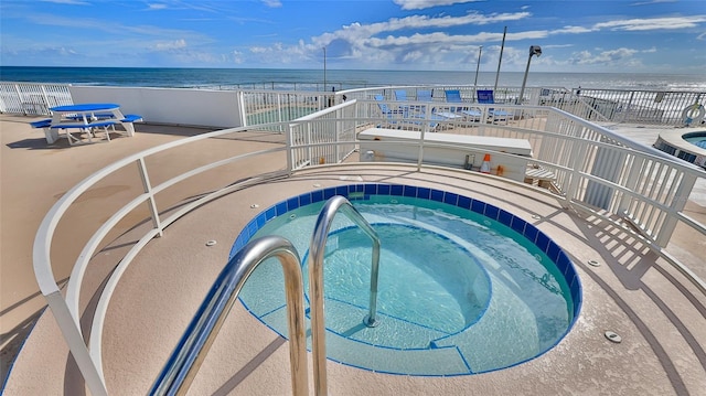 view of pool with a water view, a view of the beach, and a hot tub