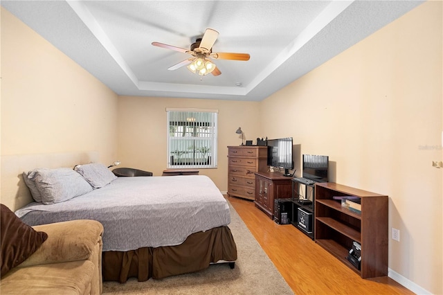 bedroom with light hardwood / wood-style flooring, a raised ceiling, and ceiling fan