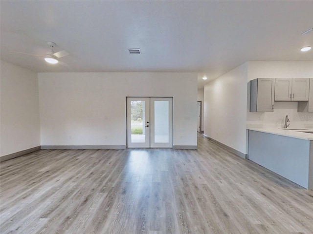 unfurnished living room with sink, french doors, light hardwood / wood-style flooring, and ceiling fan