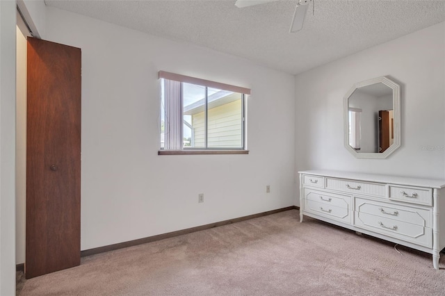 unfurnished bedroom with ceiling fan, light colored carpet, and a textured ceiling