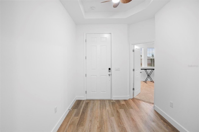 spare room with a ceiling fan, a raised ceiling, baseboards, and light wood finished floors