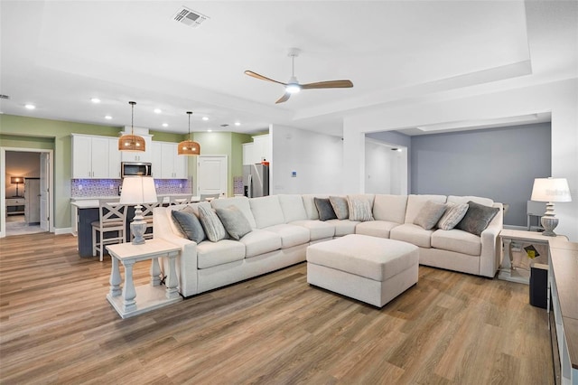 living room with light wood-style flooring, recessed lighting, a ceiling fan, visible vents, and a tray ceiling