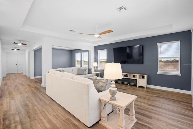 living room featuring a wealth of natural light, a raised ceiling, ceiling fan, and wood finished floors