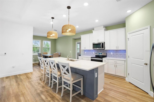 kitchen with white cabinets, appliances with stainless steel finishes, light countertops, pendant lighting, and a sink