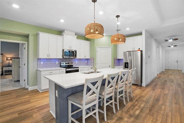 kitchen with stainless steel appliances, light countertops, white cabinetry, pendant lighting, and a sink