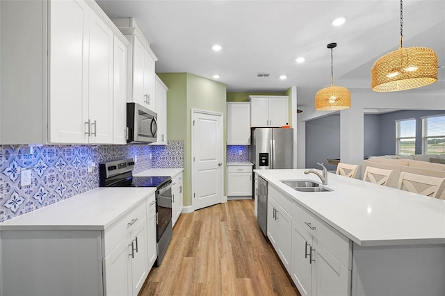 kitchen with stainless steel appliances, a sink, hanging light fixtures, light countertops, and a center island with sink