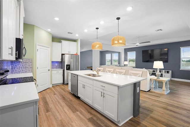 kitchen featuring decorative light fixtures, light countertops, open floor plan, white cabinets, and an island with sink