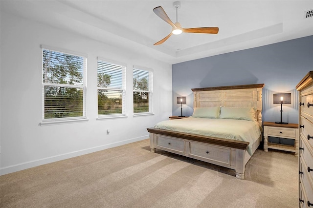 bedroom with baseboards, visible vents, a ceiling fan, light colored carpet, and a tray ceiling