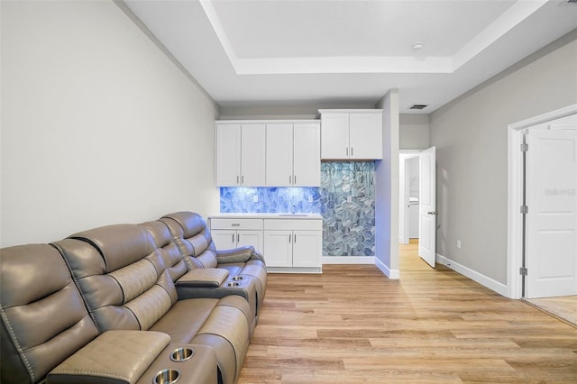 living room featuring a tray ceiling, visible vents, light wood-style flooring, and baseboards