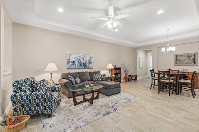 living room with a tray ceiling, ceiling fan with notable chandelier, and light wood-type flooring