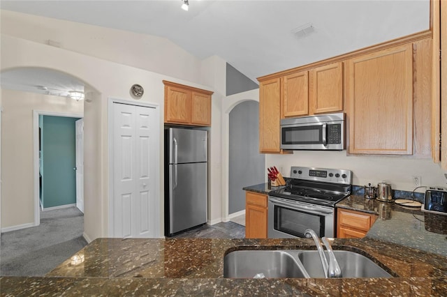 kitchen featuring appliances with stainless steel finishes, dark carpet, sink, dark stone counters, and lofted ceiling