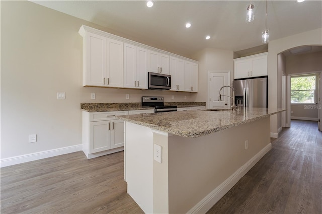 kitchen with white cabinets, stainless steel appliances, a center island with sink, and light hardwood / wood-style flooring