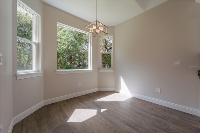 spare room featuring a chandelier, wood-type flooring, and a healthy amount of sunlight