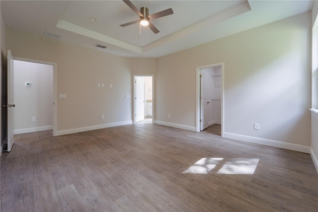 empty room featuring ceiling fan, a raised ceiling, and light wood-type flooring